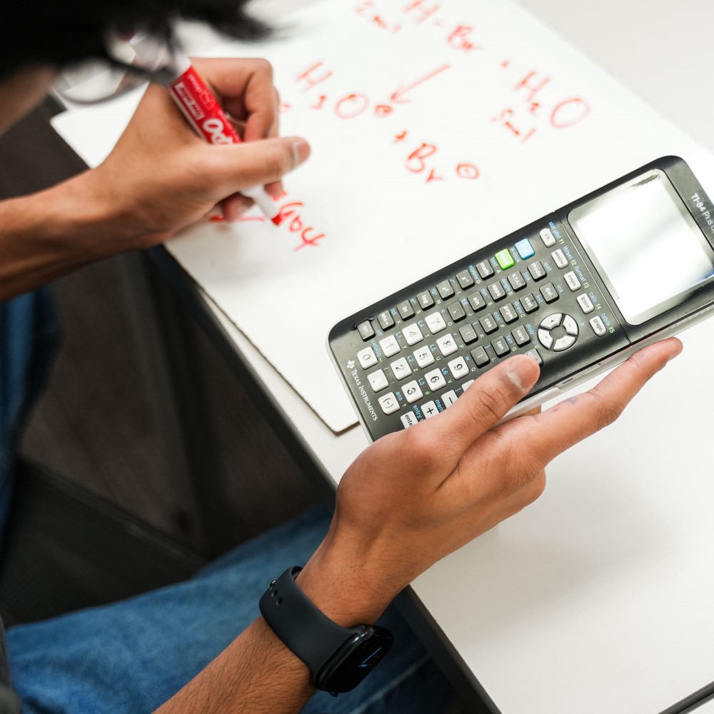Tutor holding a calculator and a marker solving problems